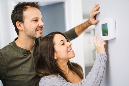happy couple adjusting thermostat